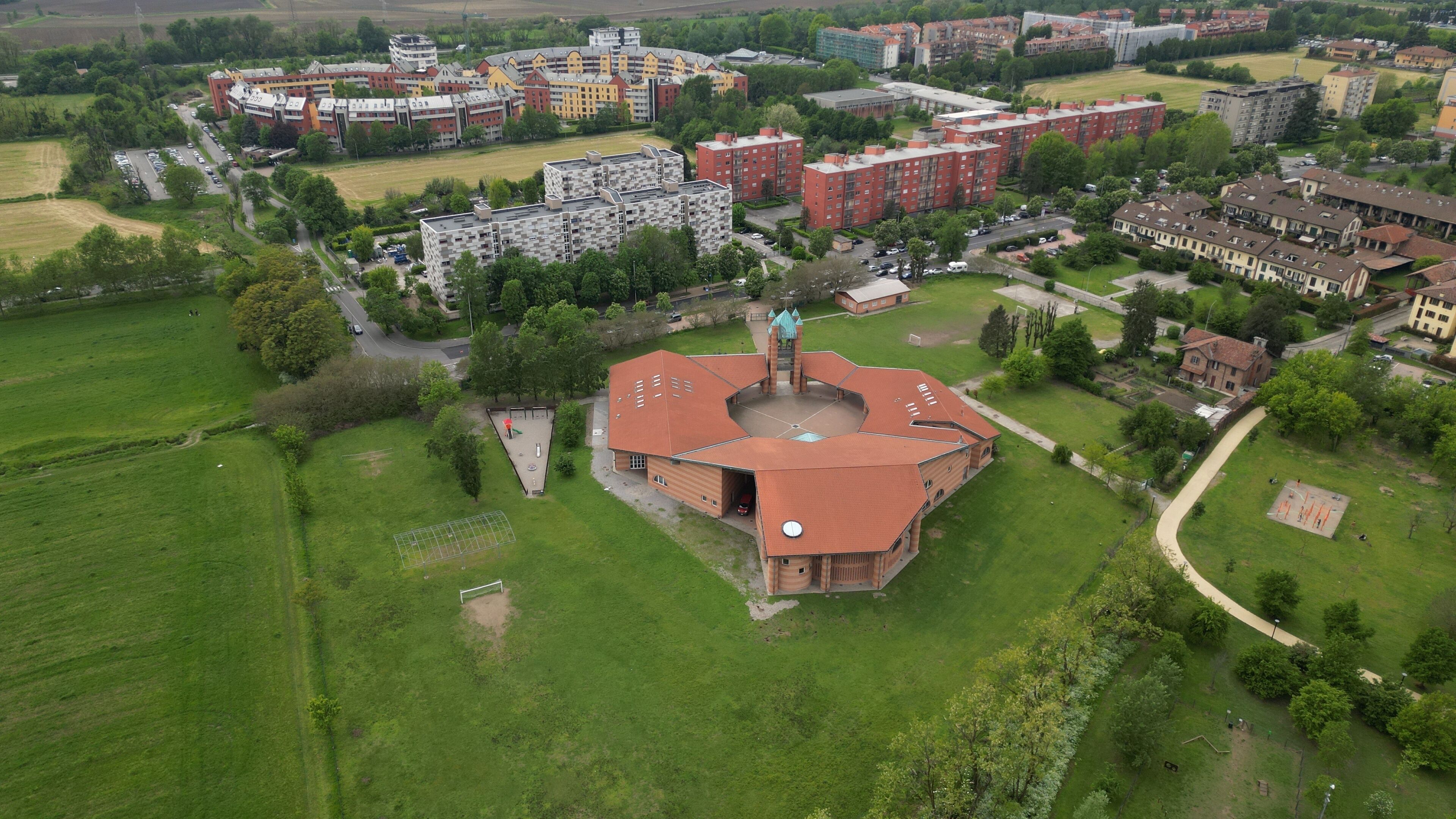 An aerial view of a campus with a central building, surrounding residential buildings, and green fields.