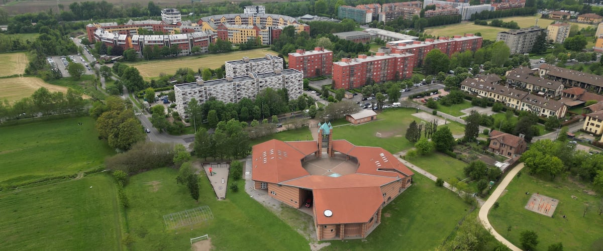 An aerial view of a campus with a central building, surrounding residential buildings, and green fields.