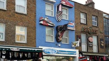 A street with shops, including a shoe store with a blue facade and a sign for 'Brandshop'.
