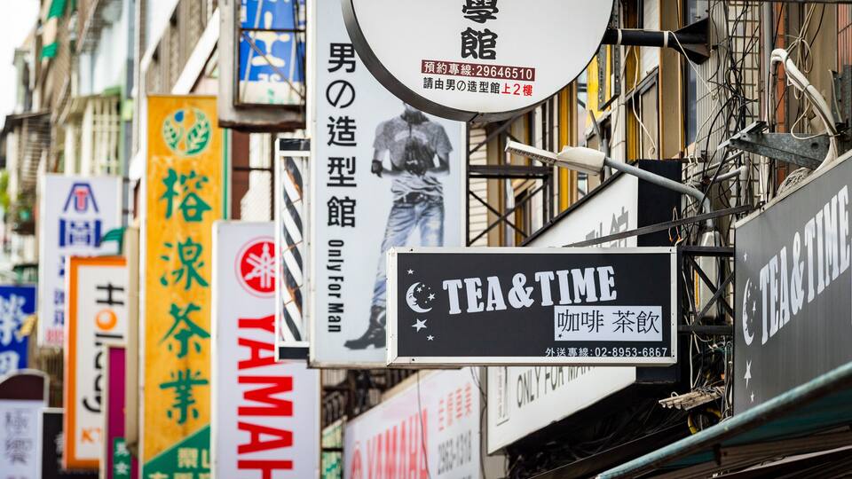 Eine Straße mit verschiedenen Schildern, darunter ein Schild mit 'TEA & TIME' und ein 'YAMAHA'-Schild.