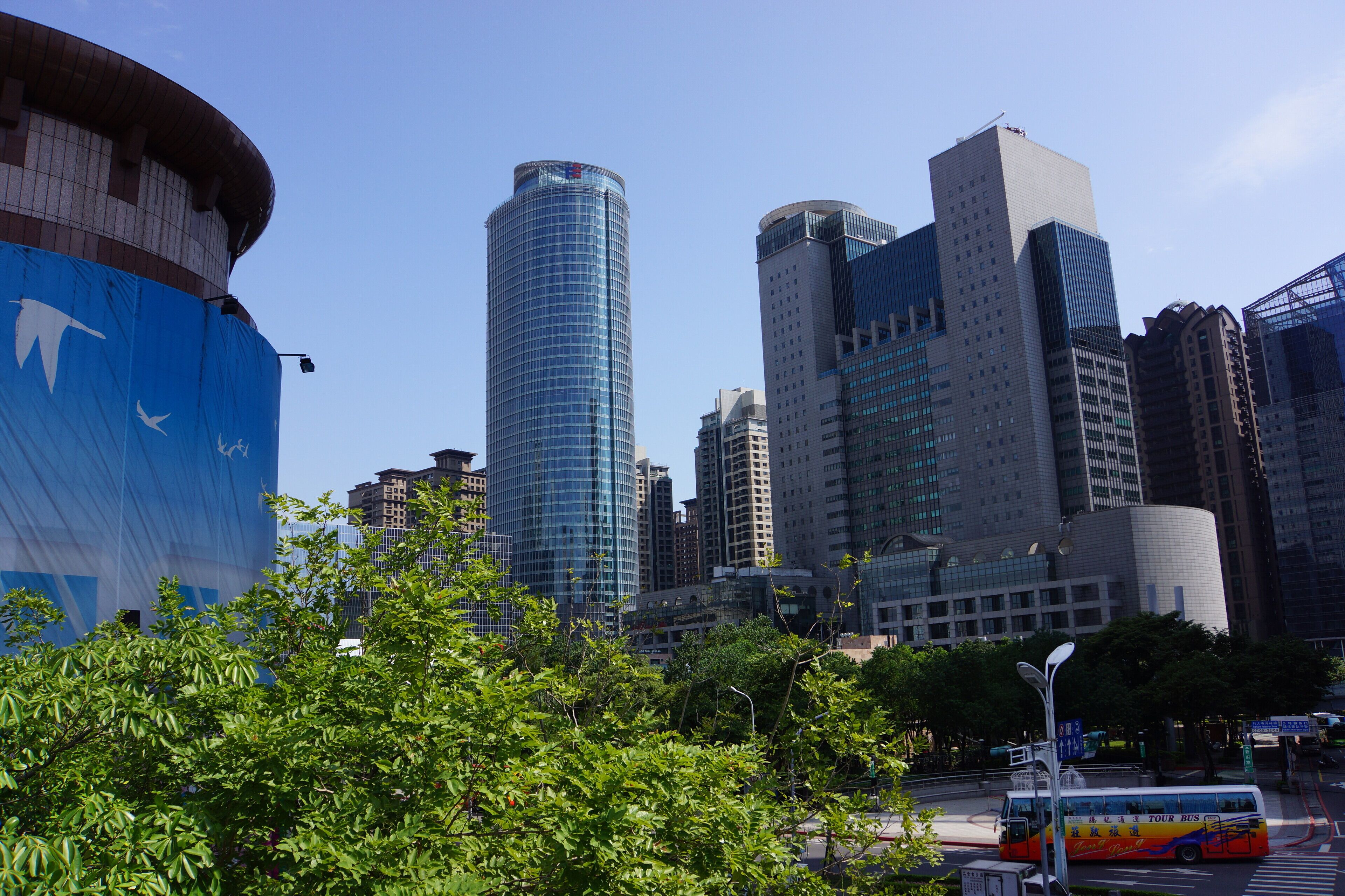A cityscape with modern skyscrapers, a large blue structure, and a tour bus.