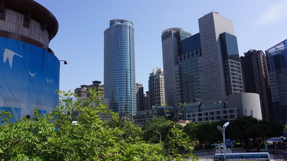A cityscape with modern skyscrapers, a large blue structure, and a tour bus.