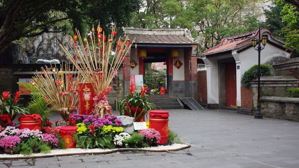 Ein traditioneller chinesischer Tempel mit roten Laternen, Räucherstäbchen und bunten Blumen.