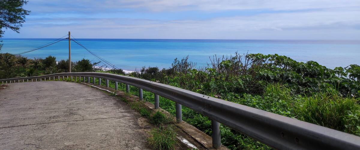 A coastal road with a metal guardrail, leading to a view of the ocean.