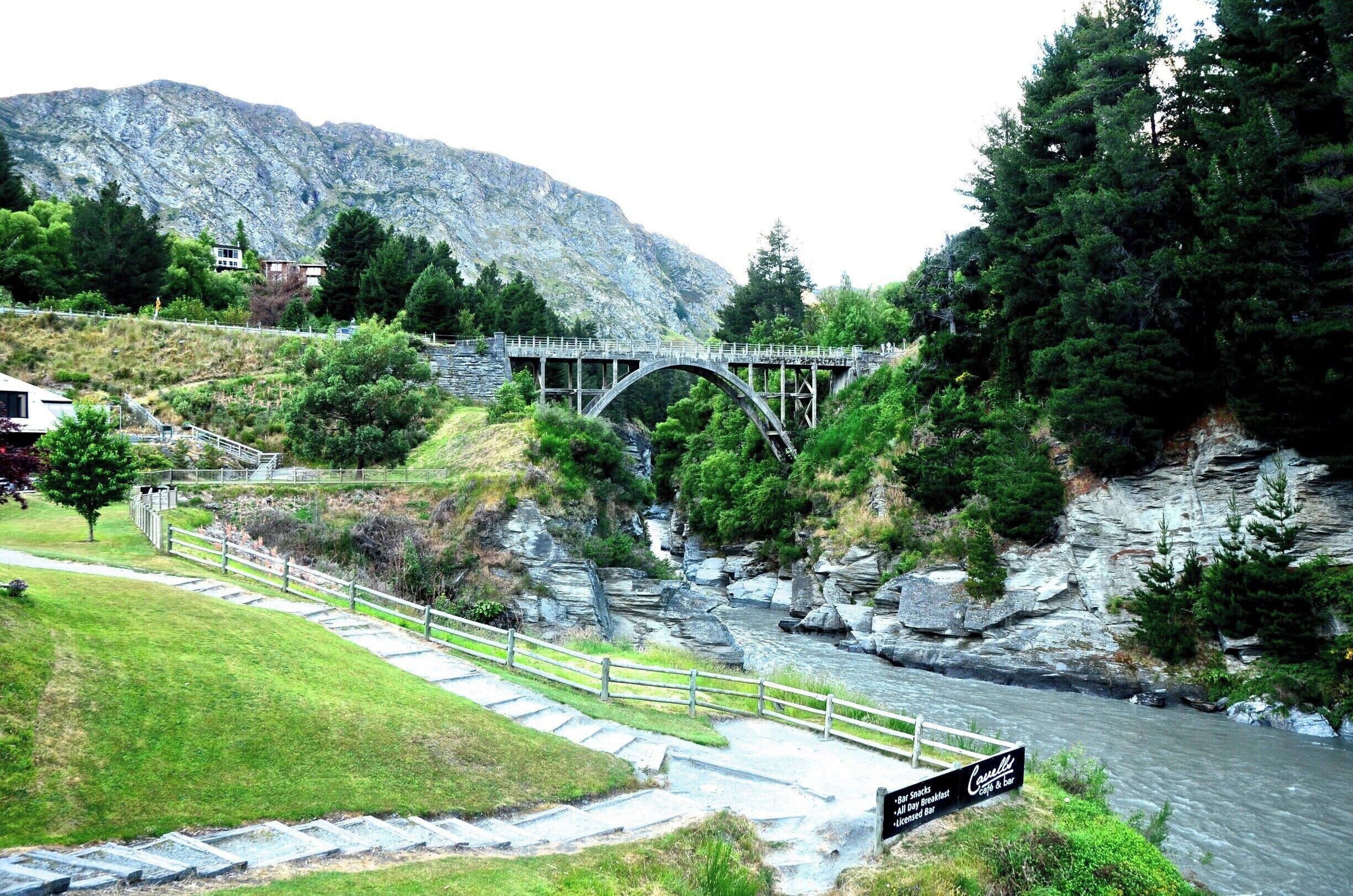 A stone bridge over a river, surrounded by greenery and mountains.