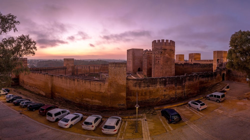 Alcalá de Guadaíra Castle: A Study in Moorish & Gothic Design, square towers, battlements sunset sky