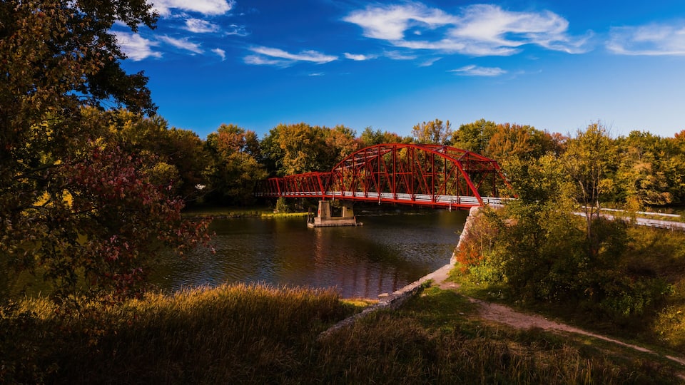 A red bridge over a river, surrounded by autumn foliage and a clear blue sky.