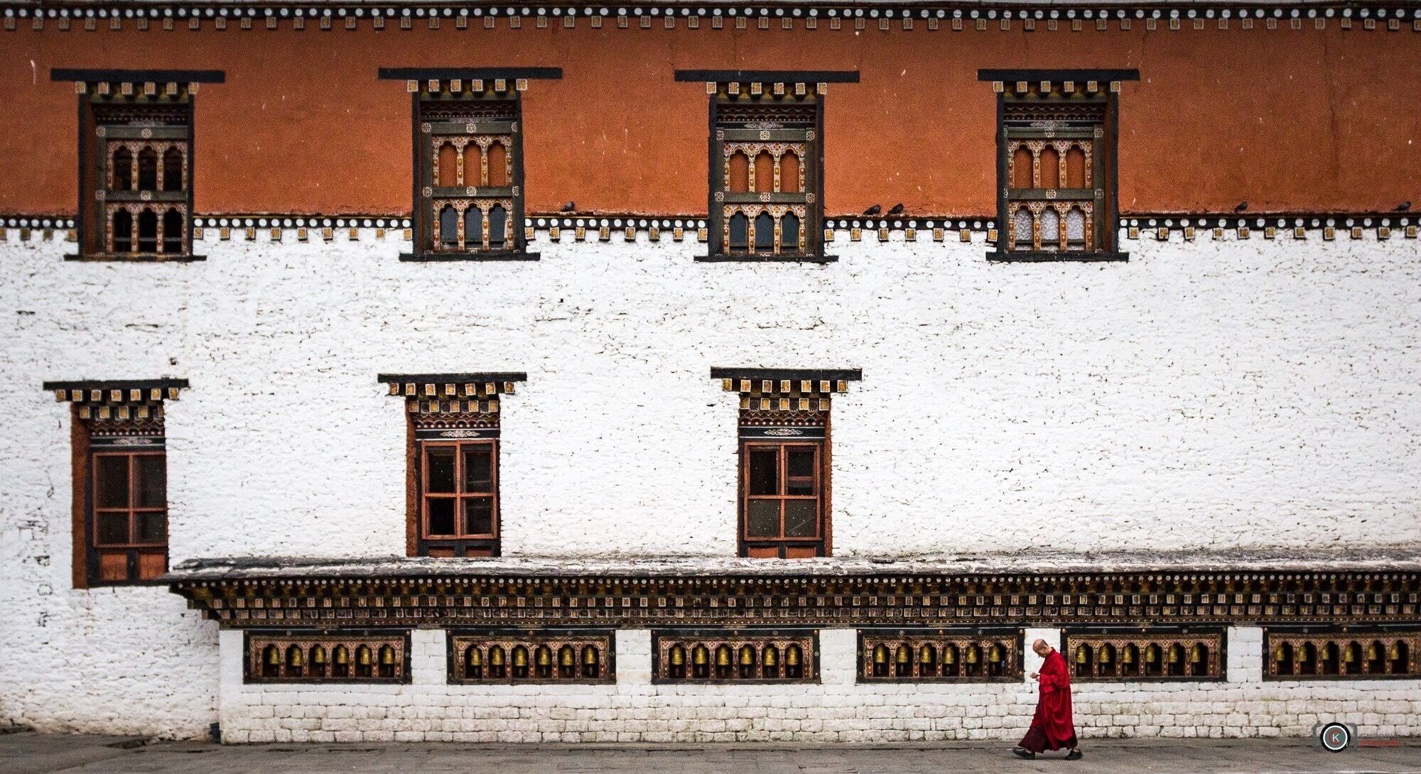 A traditional building with ornate windows and a person in a red robe walking in front.