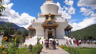 A white stupa with golden accents, surrounded by greenery and mountains.