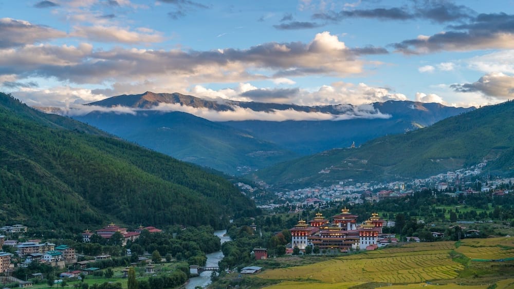 Un paysage montagneux avec des champs en terrasses, une rivière et un bâtiment traditionnel aux toits dorés.
