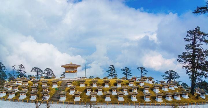 A pagoda with multiple small stupas on a hillside under a cloudy sky.