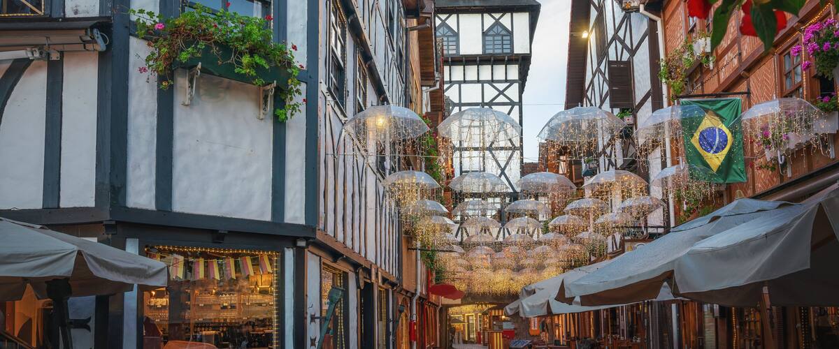 A cobblestone street lined with traditional half-timbered buildings, some with outdoor seating and umbrellas.