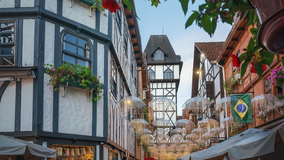 Una calle adoquinada flanqueada por edificios tradicionales con entramado de madera, algunos con mesas al aire libre y sombrillas.