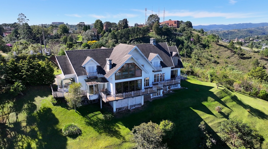 A large white house with a dark roof, surrounded by lush green grass and trees, set against a backdrop of rolling hills and distant mountains.