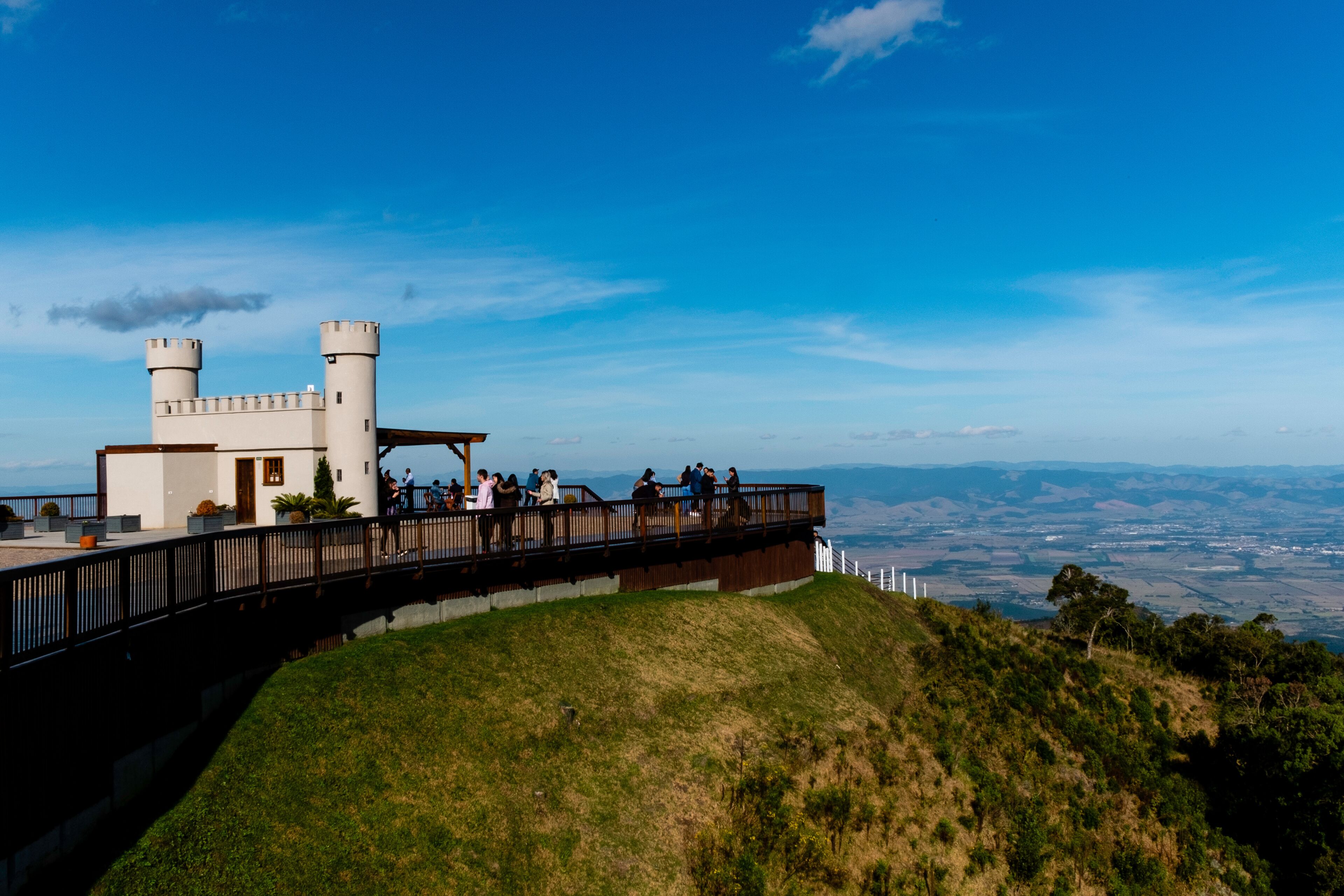 A castle-like structure with a wooden walkway, grassy hill, and a distant view of a valley.