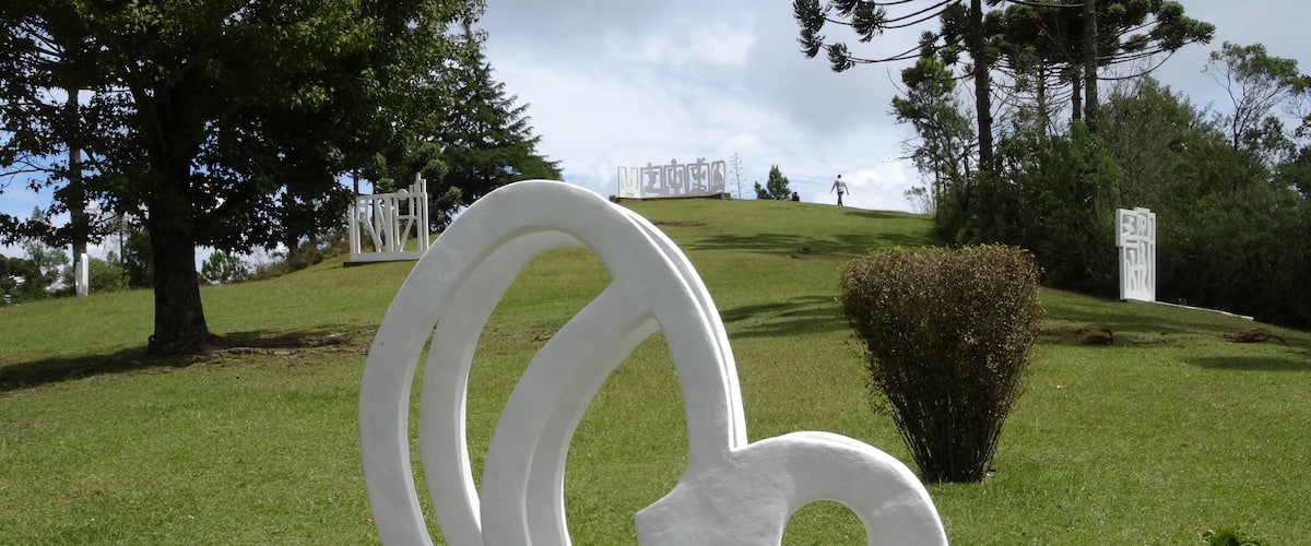 A white abstract sculpture on a grassy hill with trees and a clear sky.