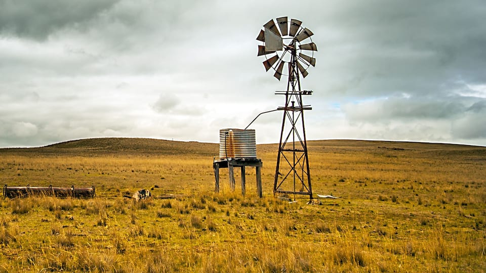 A windmill in a grassy field with a cloudy sky.