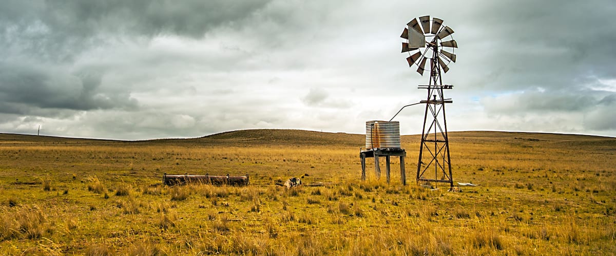A windmill in a grassy field with a cloudy sky.
