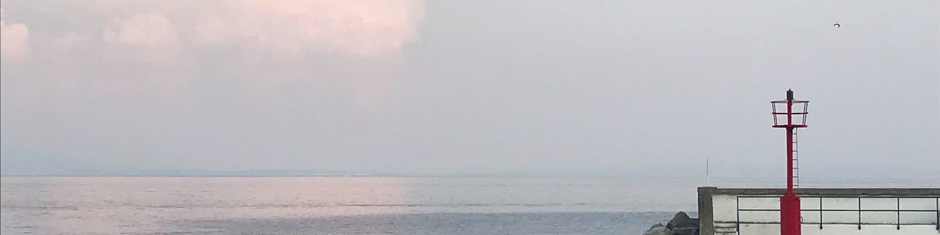 Ein ruhiges Meer mit einem roten Leuchtturm auf einem Betonsteg.