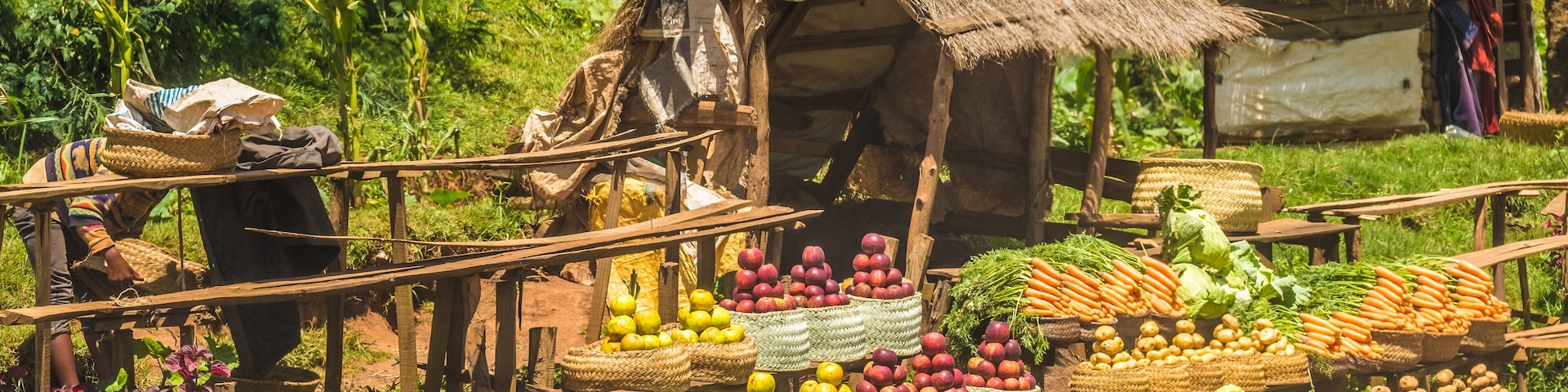 Un mercado rural con puestos de madera que exhiben frutas y verduras.
