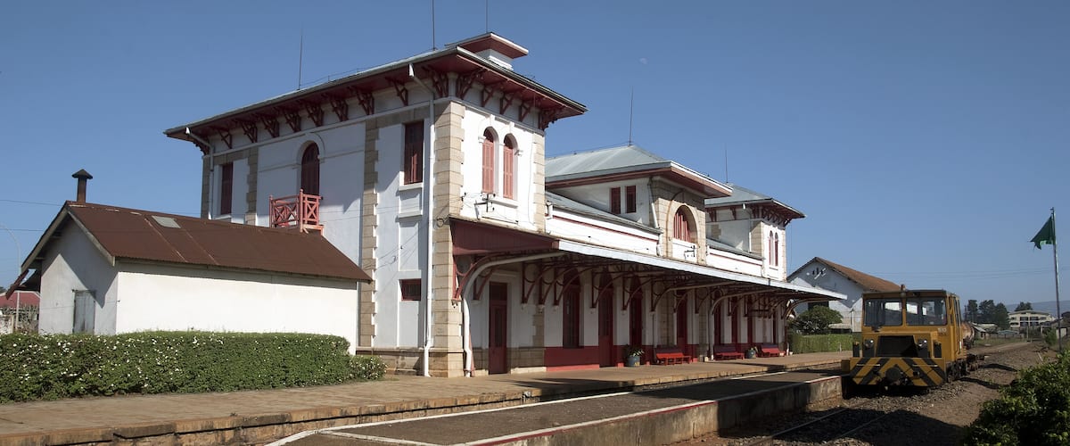 A train station with a white building, a platform, and a train on the tracks.