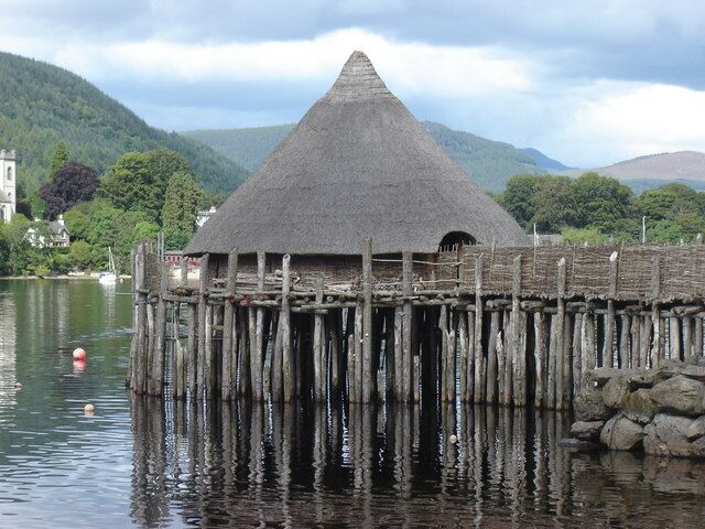 A thatched-roof structure on stilts over water, surrounded by greenery and hills.
