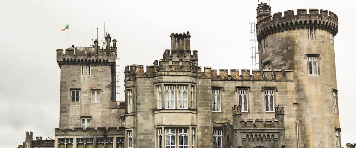 A large stone castle with multiple towers, a flag, and well-maintained gardens.