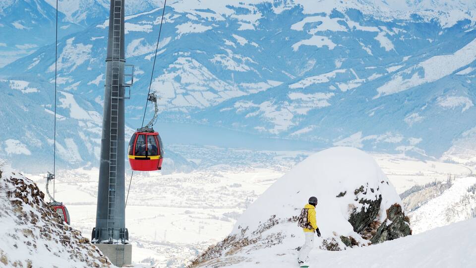 A snowy mountain landscape with a cable car system, a person in a yellow jacket, and a large snow-covered mound.
