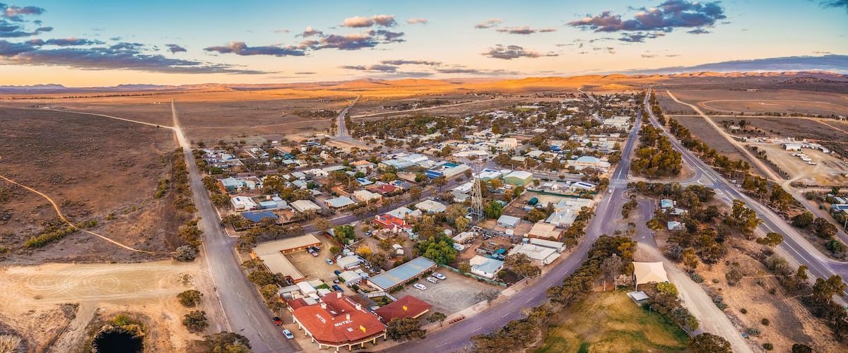 An aerial view of a town with a prominent road, a body of water, and surrounding hills.
