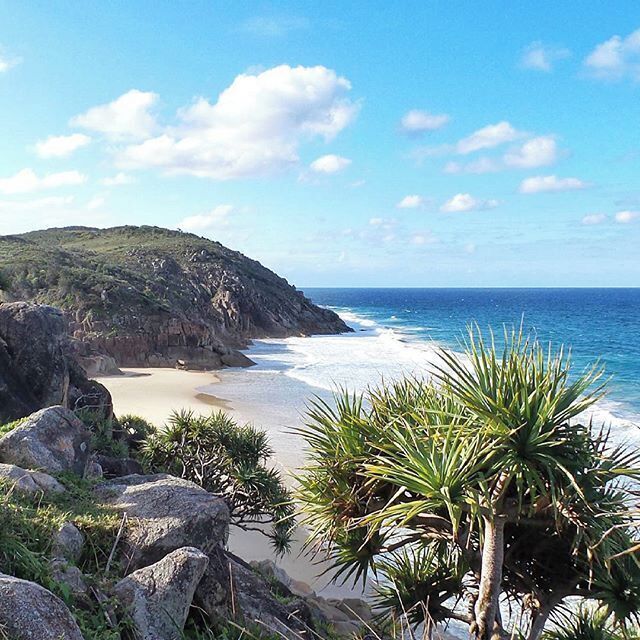 A coastal landscape with a sandy beach, rocky cliffs, and a clear blue sky.