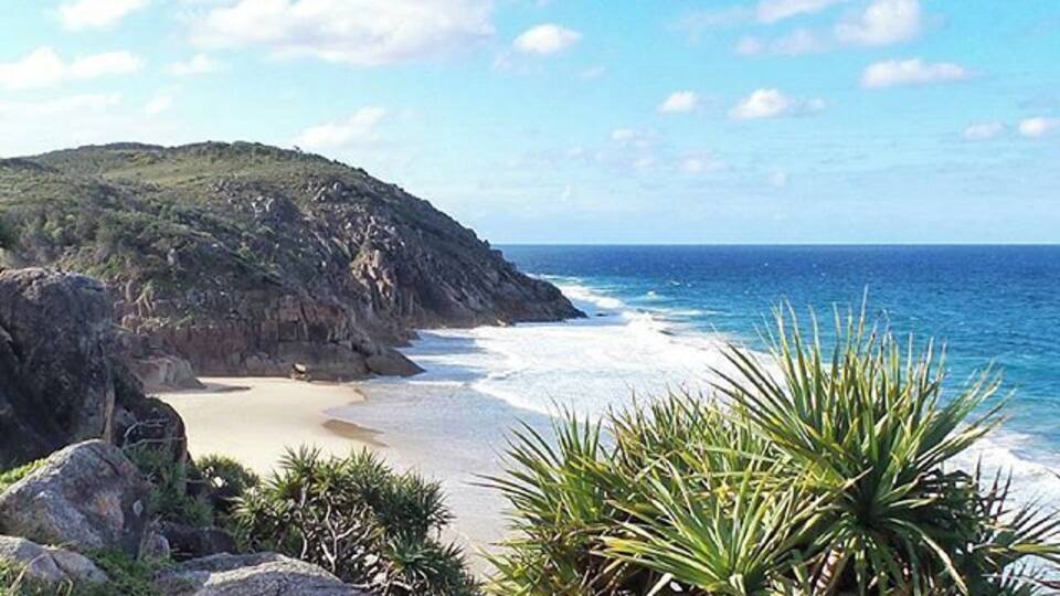A coastal landscape with a sandy beach, rocky cliffs, and a clear blue sky.