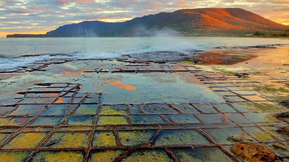 A salt flat with a grid pattern, surrounded by mountains and a sunset sky.