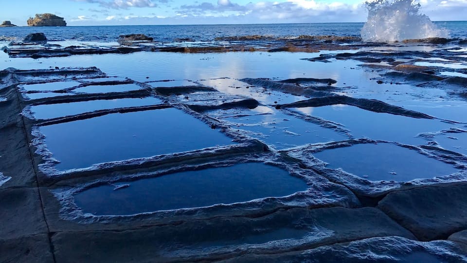 A rocky shoreline with clear blue water and a splash of water.