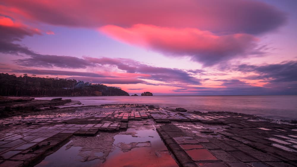 Un paysage côtier avec un ciel au coucher du soleil, une côte rocheuse et une mer calme.
