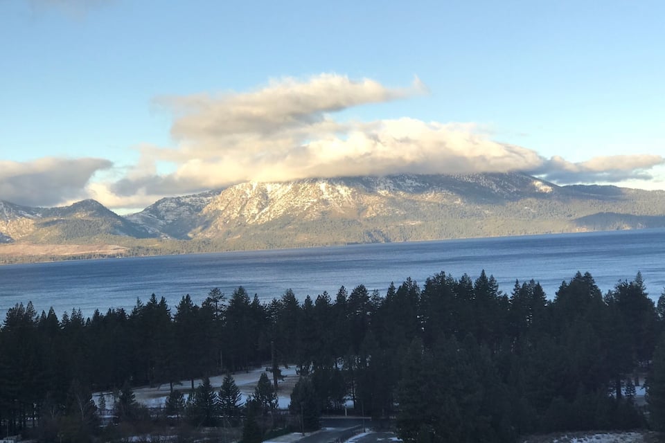 A mountain range with a lake in the foreground and a forested area in the midground.