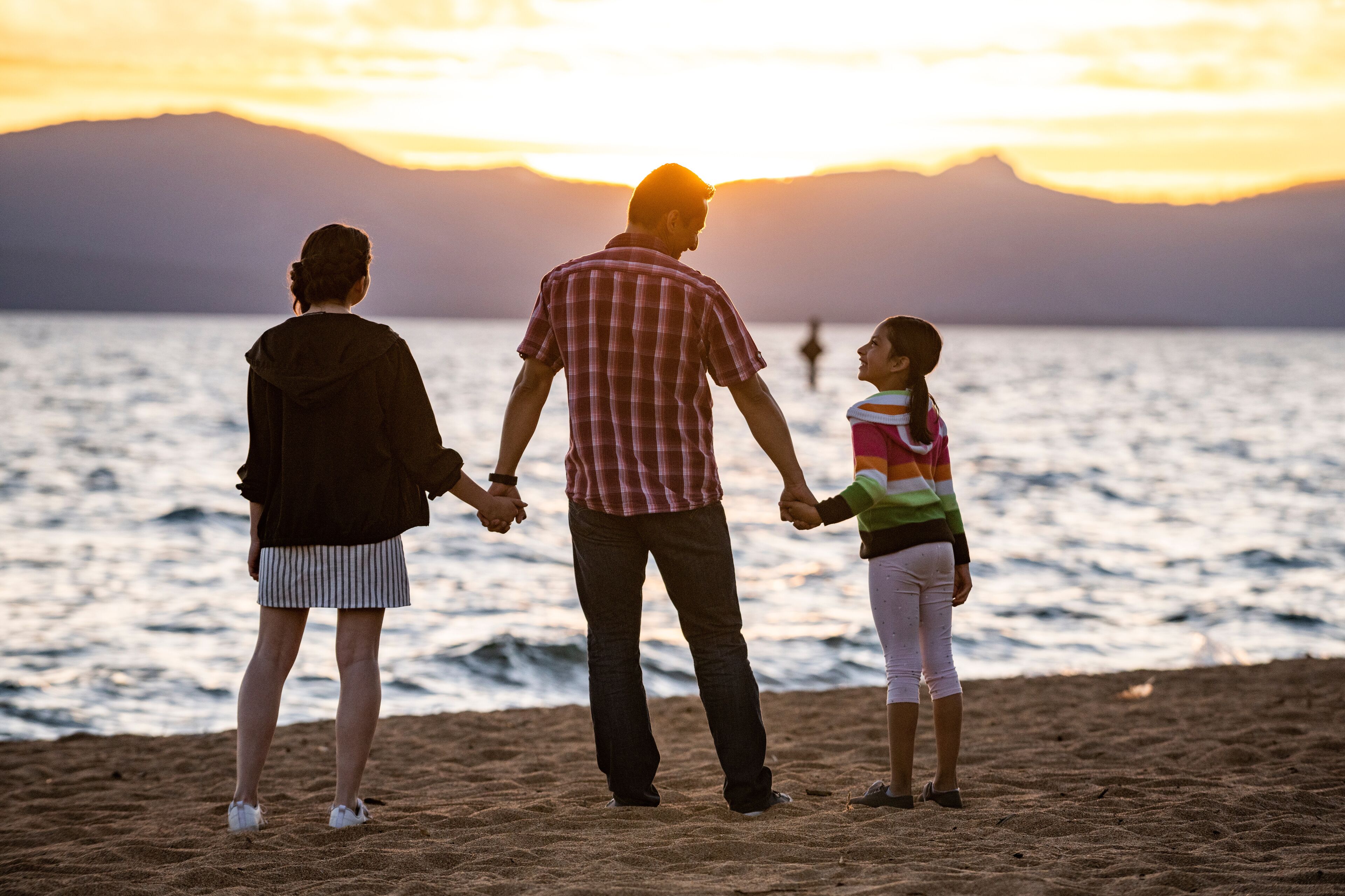 A dad and his daughters watch sunset on the beach in Lake Tahoe, NV