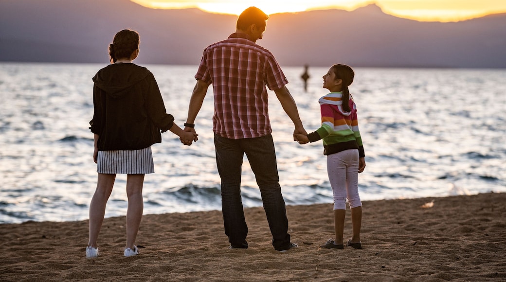 A dad and his daughters watch sunset on the beach in Lake Tahoe, NV