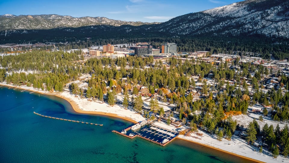 A coastal town with a marina, snow-covered mountains, and dense forests.