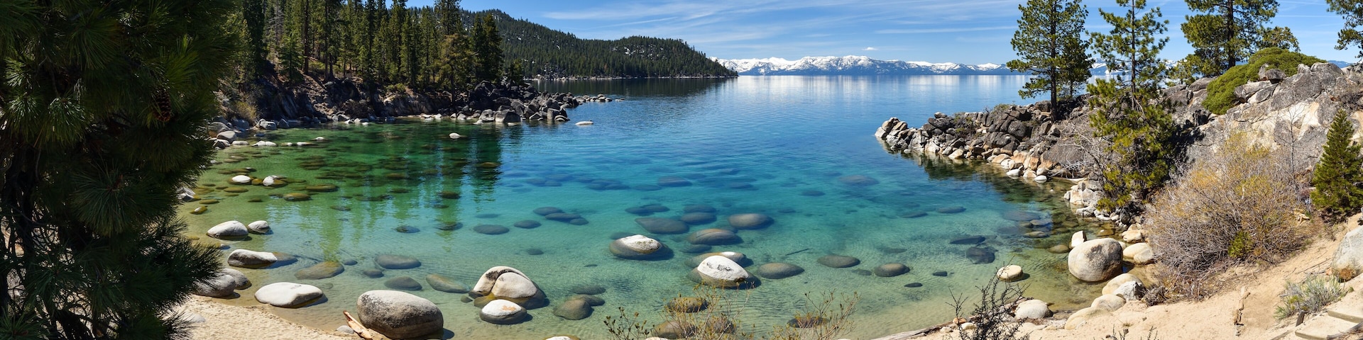 Un lago tranquilo rodeado de orillas rocosas y densos pinos.