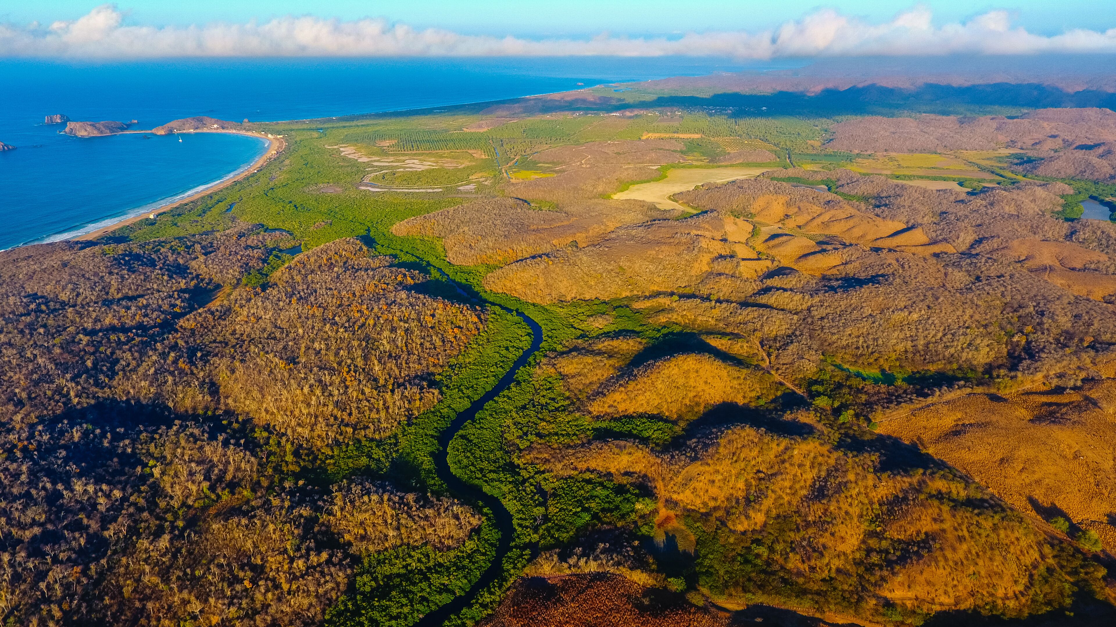 A coastal landscape with a winding river, green vegetation, and a beach.