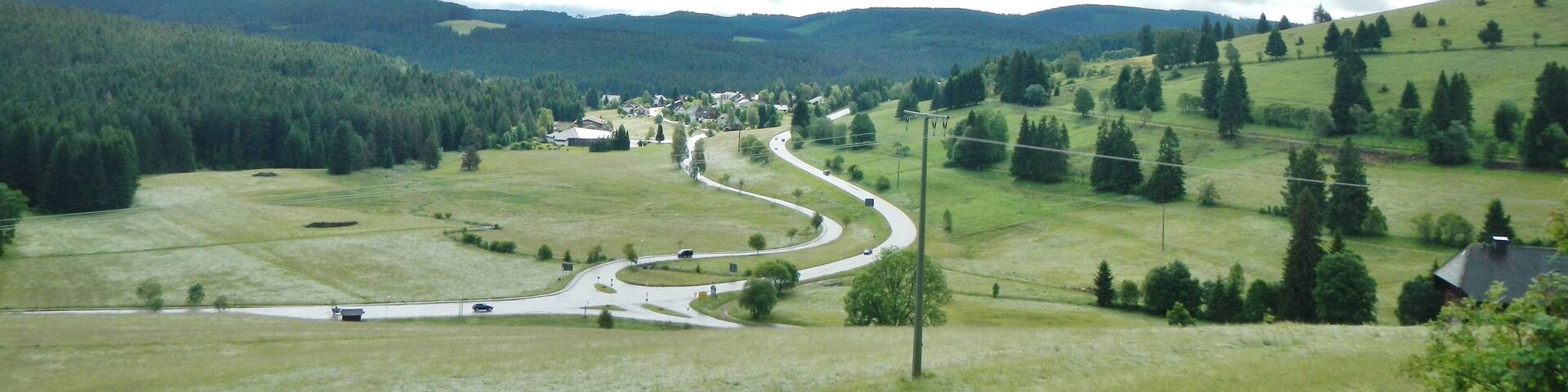 A winding road through a hilly landscape with scattered houses and dense forests.