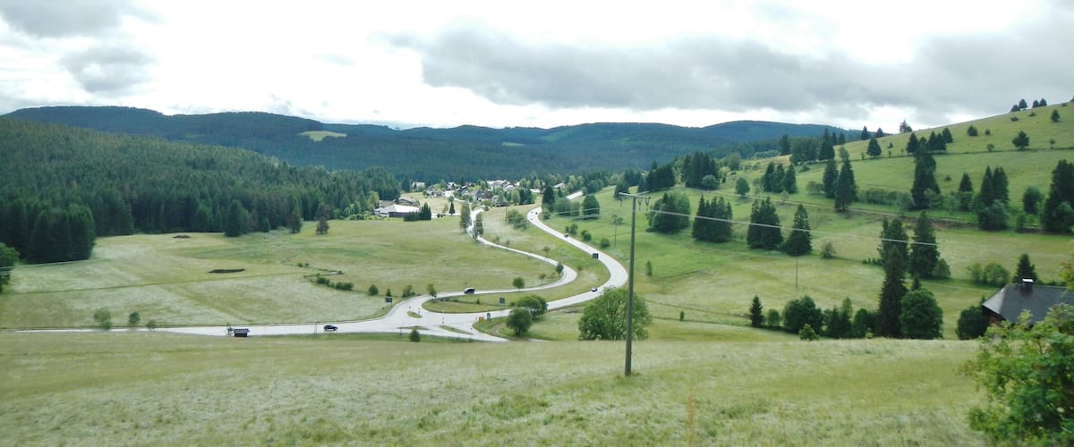 A winding road through a hilly landscape with scattered houses and dense forests.