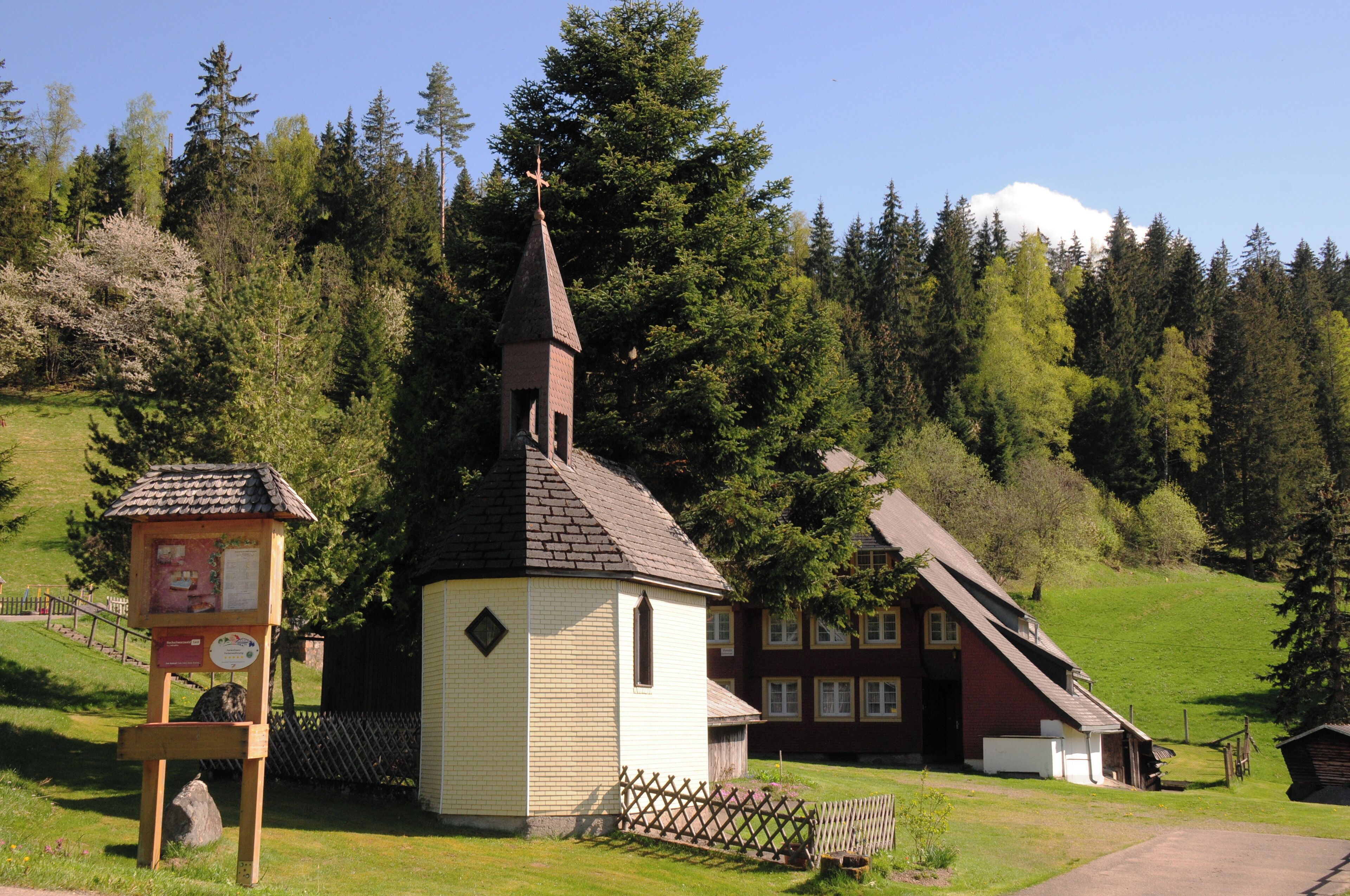 A church with a steeple, a small wooden structure with a sign, and a red house with a sloped roof.