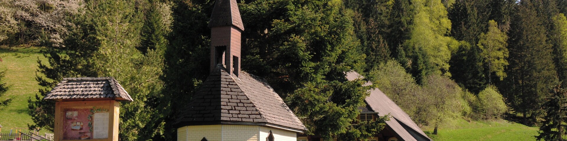 A church with a steeple, a small wooden structure with a sign, and a red house with a sloped roof.