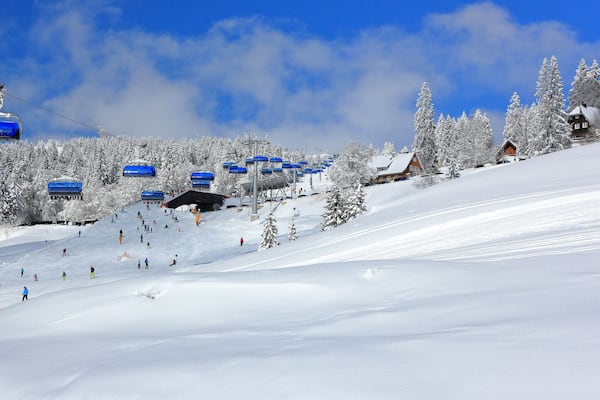 Ein verschneiter Ski-Hang mit einer Seilbahn, schneebedeckten Bäumen und einem roten Gebäude.