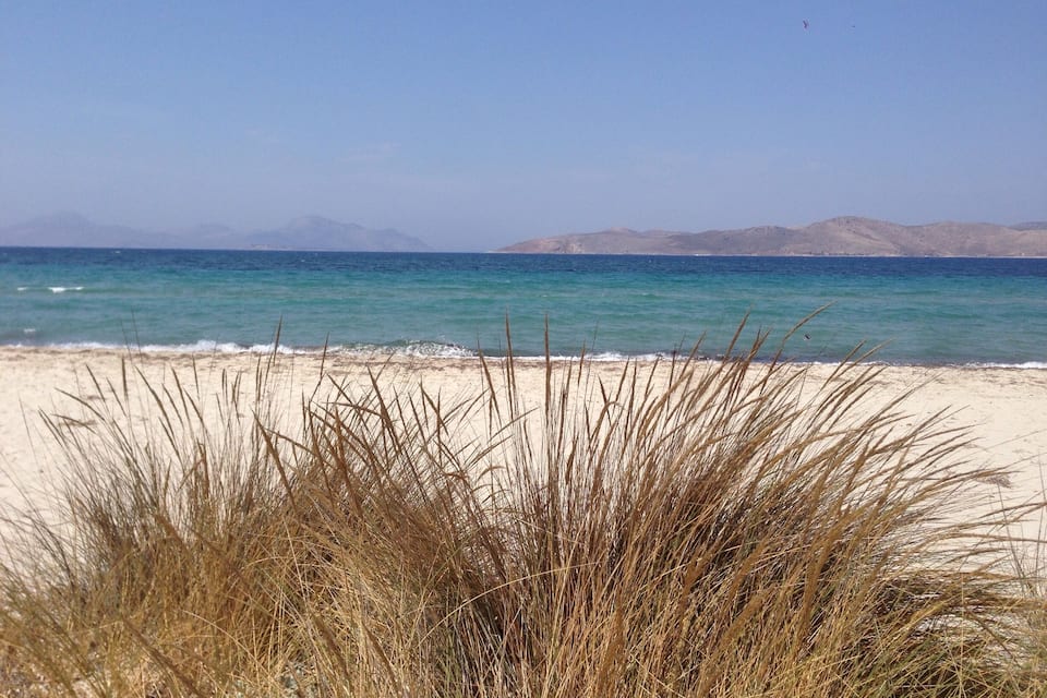 Een strand met helder turquoise water en verre bergen.