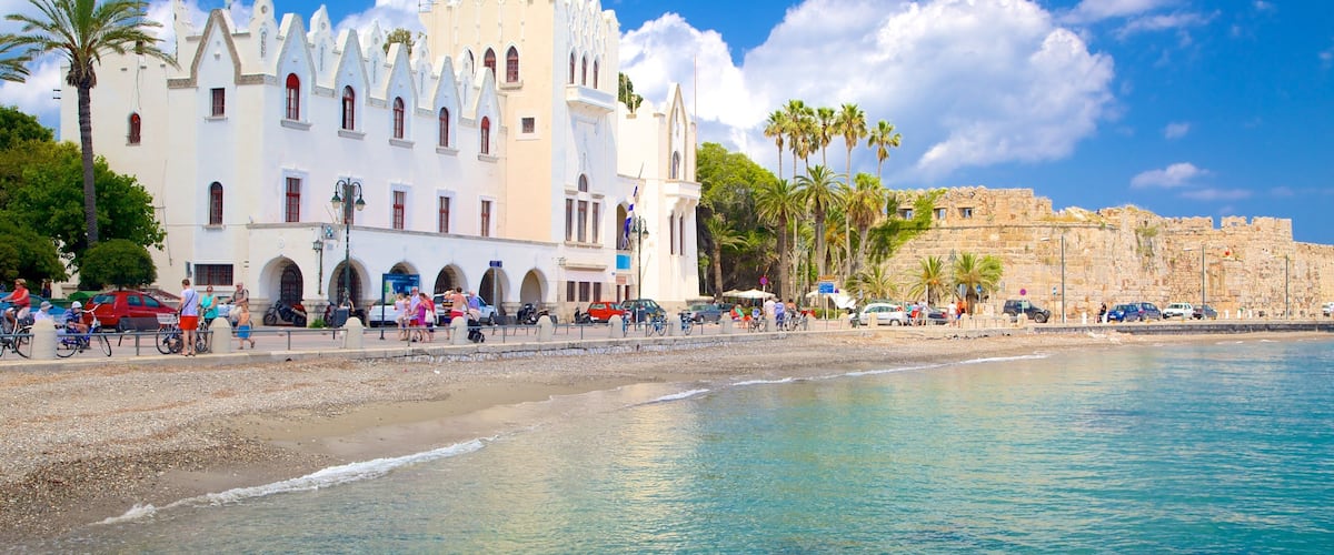 A coastal town with a prominent white building with a clock tower, palm trees, and a historic stone wall.