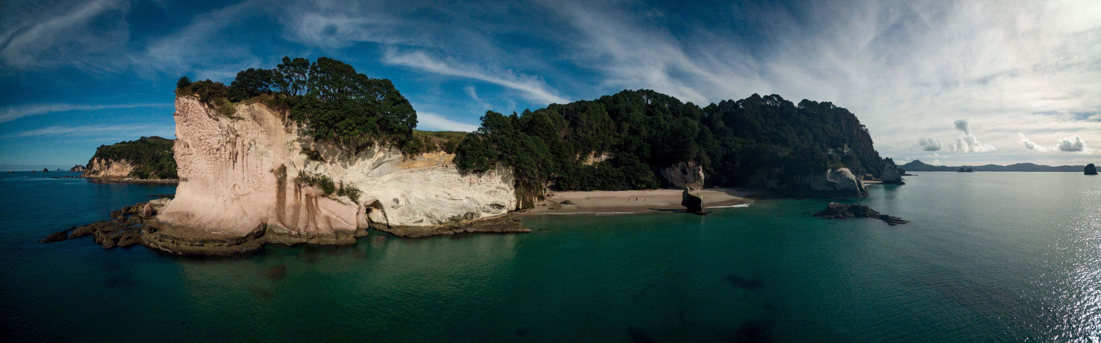 A coastal landscape with a prominent white cliff, a sandy beach, and a forested island.