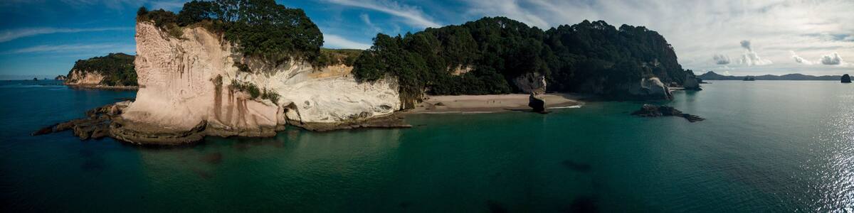 A coastal landscape with a prominent white cliff, a sandy beach, and a forested island.