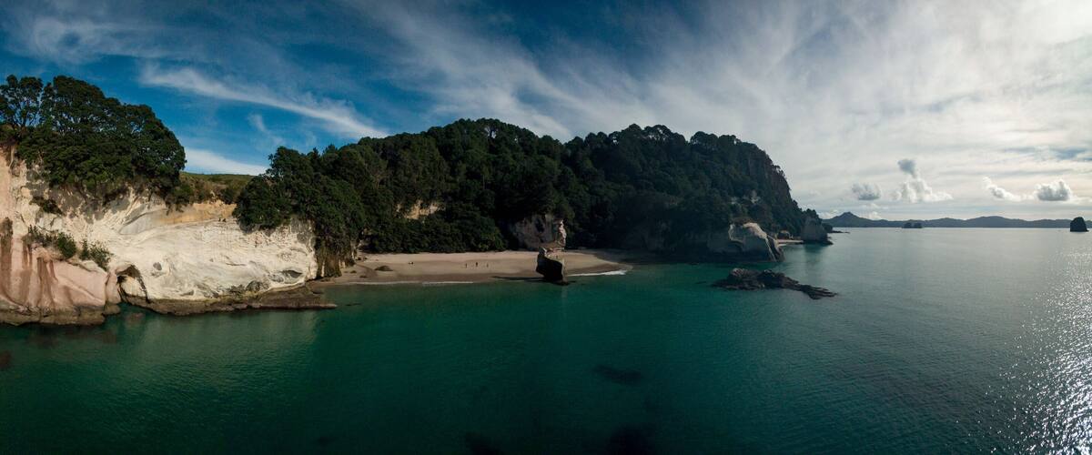 Eine Küstenlandschaft mit einer markanten weißen Klippe, einem Sandstrand und einer bewaldeten Insel.